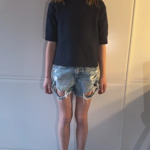 Blå jeansshorts med slitna detaljer - Snygga blå jeansshorts med slitna detaljer och fransar. Perfekta för en avslappnad stil. De har en klassisk femficksdesign och knappgylf.