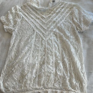 Vit spetsblus med korta ärmar - Säljer en elegant vit spetsblus med korta ärmar och vackra spetsdetaljer. Blusen har ett dekorativt mönster framtill och en rund halsringning. Perfekt för en stilren look. ❤️