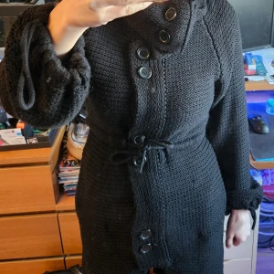 Långkofta svart nyskick  - En superfin svart kofta från Sara Kelly, koftan har legat nedpackad så kommer att rolla av den innan ev försäljning.  Den har både knappar, fickor och snörning . Kragen kan man ta bort då den sitter med knappar, såg en tråd(se sista bild) men kan lösa det med att fixa så den kommer på insidan. Som sagt den har legat nedpackad och bilderna gör sig inte riktigt men den är annars I nyskick förutom denna tråd som finns. Strl 38-40.  Nypris 799 kr