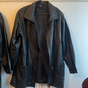 Svart skinnjacka - Snygg svart skinnjacka med dragkedja och dekorativa sömmar. Jackan har långa ärmar och praktiska fickor framtill. Perfekt för en cool och stilren look.