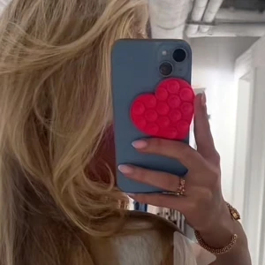 Röd hjärtformad  - Säljer endast det röda hjärtat/extra kostnad 10kr för ett iPhone 12 skal Säljer en röd hjärtformad som kan fästas på baksidan av en mobiltelefon. . Den är lätt att ta av och på och ger din telefon en personlig touch.