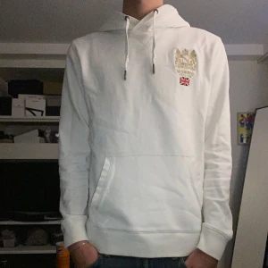 Vit hoodie från Morris - Säljer en stilren vit hoodie från Morris med detalj vid bröstet. Killen på bilden är 175 och skulle säga att den passar på någon mellan 165-177. Bra skick och väldigt bekväm. Storlek S. Hör av dig vid frågor