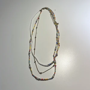 Flerfärgat pärlhalsband - Charmigt flerfärgat halsband med små pärlor i olika färger och vita inslag. Halsbandet har en justerbar kedja och ett klassiskt klolås. Perfekt för att ge en färgglad touch till din outfit.