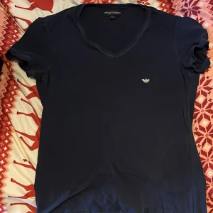 Mörkblå t-shirt från Emporio Armani - Snygg mörkblå t-shirt från Emporio Armani med v-ringning och korta ärmar. Diskret logga på bröstet. Perfekt för en stilren look.