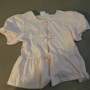 Ljusrosa blus från Gina Tricot - Söt ljusrosa blus från Gina Tricot med korta puffärmar och knytband framtill. Jag har inte använt den här tröjan någon gång då jag inte tycker att jag passar i den💞