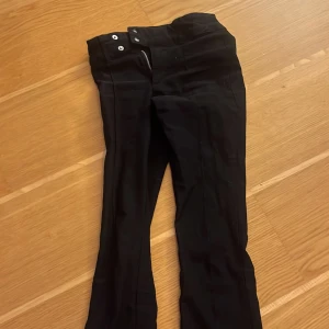Svarta byxor med dragkedja och knappar - Snygga svarta byxor med mid waist och stilrena detaljer som dragkedja och knappar. Perfekta.