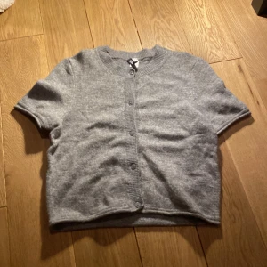 Grå kofta från Divided H&M - Säljer en mysig grå kofta från Divided H&M. Den har korta ärmar och knappar framtill. Perfekt svalare dagar.