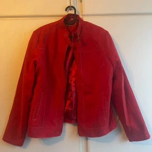 Röd mockajacka från Biaggini - Snygg röd mockajacka från Biaggini med dragkedja och spänne vid halsen. Jackan har en stilren design med långa ärmar och diskreta sömmar som ger en elegant look. Perfekt för att ge din outfit en färgklick.