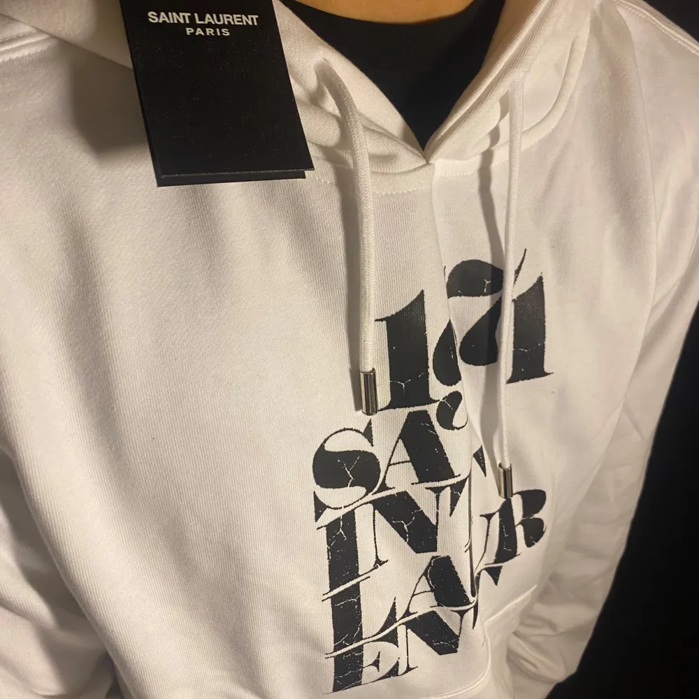 Säljer min väns snygga vita hoodie från Saint Laurent med tryck framtill. Den har en klassisk passform med långa ärmar och en bekväm huva med dragsko. Perfekt för en stilren och avslappnad look. Passar både till vardags och festliga tillfällen. Hör av dig vid frågor o funderingar!. Tröjor & Koftor.