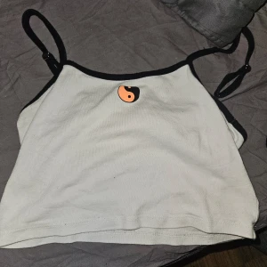 Vit och svart linne från Divided - Säljer en snygg vit linne från Divided med svarta kanter och justerbara axelband. Den har en cool yin-yang-symbol på framsidan. Perfekt för sommardagar eller som ett lager under en jacka. Använd ett par gånger men i bra skick!