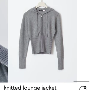 Grå stickad loungejacka helt nytt sett - Mysig grå stickad loungejacka med dragkedja och huva. Perfekt för avslappnade dagar hemma eller en chill dag ute. Den har långa ärmar och ribbade detaljer vid ärmslut och nederkant för extra komfort.