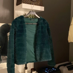 Mörkgrön pälsjacka från Gina Tricot - Säljer en supermjuk och fluffig mörkgrön pälsjacka från Gina Tricot. Perfekt för att hålla sig varm och stilren under kyliga dagar. Jackan har långa ärmar och en öppen design utan knappar eller dragkedja. Den är i mycket bra skick och redo för nya äventyr! 💚man kan stänga den det är liten knapp inom i jackan 