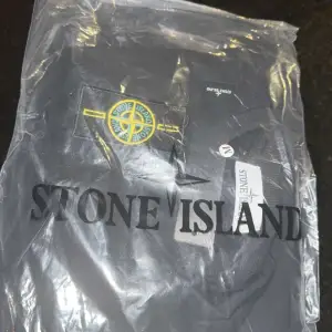 Säljer en stilren svart tröja från Stone Island i storlek M. Tröjan har en klassisk design med rund hals och långärmade ärmar. Den ikoniska Stone Island-loggan sitter på ärmen. Perfekt för både vardag och fest!