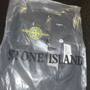 Svart tröja från Stone Island - Säljer en stilren svart tröja från Stone Island i storlek M. Tröjan har en klassisk design med rund hals och långärmade ärmar. Den ikoniska Stone Island-loggan sitter på ärmen. Perfekt för både vardag och fest!