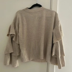 Beige ribbad tröja med volangärmar - Säljer en superfin beige tröja med ribbad struktur och volangdetaljer på ärmarna. Perfekt för höst och vår! Den har en lös passform och är riktigt bekväm att ha på sig. Passar både till vardags och lite finare tillfällen. 🧡