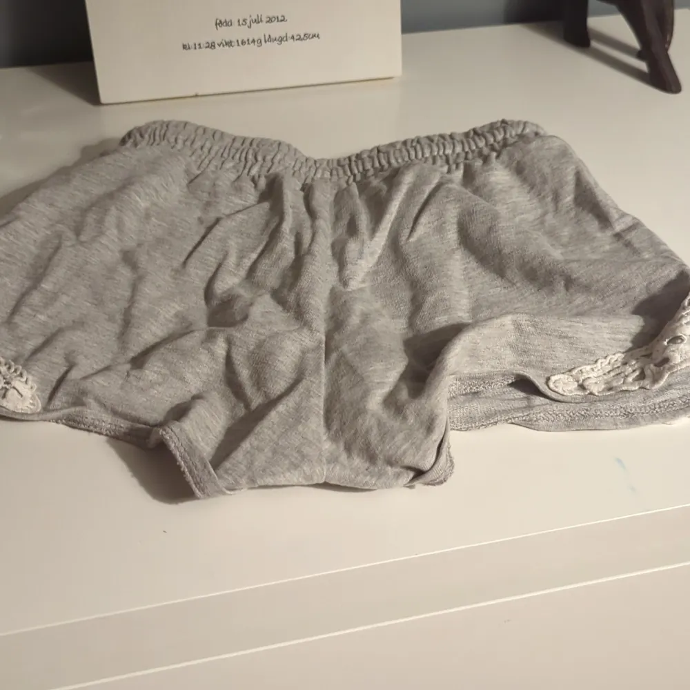 Säljer ett par superbekväma grå shorts med elastisk midja och snörning. De har fina vita spetsdetaljer på sidorna som ger en söt touch. Perfekta för en avslappnad dag hemma eller en somrig utflykt. Materialet känns mjukt och skönt mot huden.. Shorts.