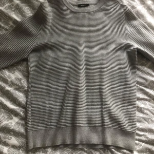 Grå stickad tröja Lindeberg  - Säljer en stilren grå stickad tröja i mycket bra skick. Den har en klassisk rund hals och långa ärmar, perfekt för kyliga dagar. Tröjan är mjuk och bekväm, idealisk för både vardag och avslappnade tillfällen. Passar perfekt till jeans eller chinos!