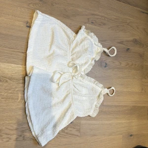 Vit linne med volangdetaljer - Säljer en söt vit topp med volangdetaljer och smala axelband. Toppen är ärmlös och har en luftig passform, perfekt för varma sommardagar. Den är gjord i ett mjukt och bekvämt material.