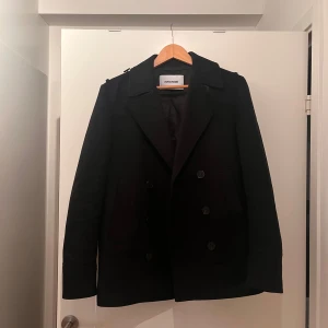 Svart kappa från Zadig & Voltaire - Säljer en stilren svart kappa från Zadig & Voltaire i storlek 46. Den har en klassisk design med knappar framtill och är perfekt för både höst och vinter. Kappan är i mycket bra skick och passar perfekt för en elegant look. Kappan är köpt utomlands av min farsa för 590 euro vilket motsvarar nästan 7000 kr