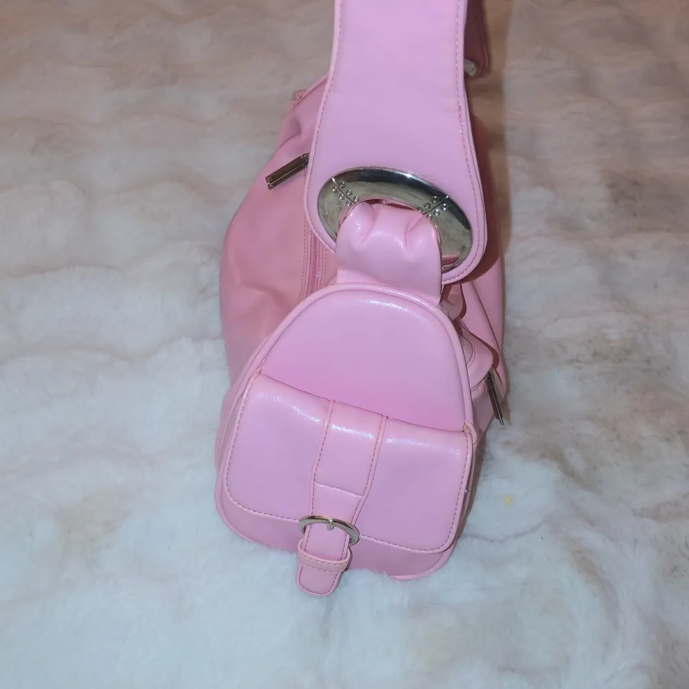 Säljer en superfin rosa axelväska i syntetmaterial. Väskan har en cool design med stora silverringar och en praktisk dragkedja framtill. Perfekt för att liva upp vilken outfit som helst! 💖. Laukut & Käsilaukut.