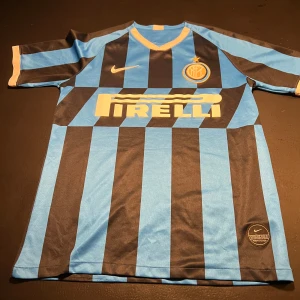 Inter Milan fotbollströja - Säljer en klassisk Inter Milan fotbollströja från Nike i svart och blått randigt mönster. Tröjan har korta ärmar och Pirelli-loggan på framsidan. Perfekt för fans av laget eller samlare av fotbollströjor!