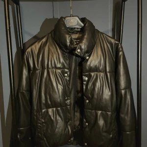 Svart pufferjacka från Vero Moda - Säljer en snygg svart pufferjacka från Vero Moda i mycket bra skick. Jackan har en glansig finish och stängs med knappar. Perfekt för kyliga dagar och ger en cool look. Passar bra till både vardag och fest!