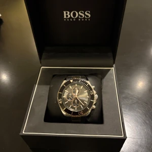 Hugo Boss klocka i guld och svart (ocean edition) - Säljer en stilren Hugo Boss klocka i guld/brons med svarta detaljer. Klockan har en elegant design med en svart urtavla och guldiga/bronsiga detaljer. Den kommer i originalförpackning och är i mycket bra skick. Perfekt för både vardag och fest! Den perfekta julklappen!