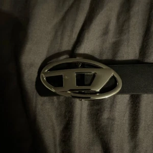 Svart diesel bälte med silverfärgat spänne - Säljer ett stilrent svart bälte med ett coolt silverfärgat spänne. Perfekt för att ge din outfit en extra touch. Bältet är i bra skick och passar till både vardag och fest. Ett måste i garderoben för den modeintresserade!