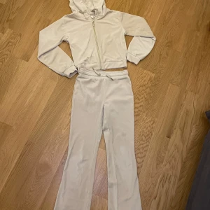 Beige hoodie och byxor från Gina Tricot - Säljer ett set med en beige hoodie och matchande byxor från Gina Tricot. Hoodien har dragkedja och långa ärmar, perfekt för en avslappnad stil. Byxorna är bekväma och har en normal passform. Perfekt för mysiga dagar hemma eller en chill dag ute.