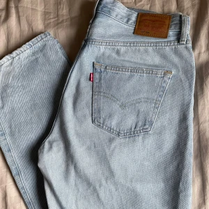 Levi's 501 ljusblå jeans - Säljer ett par klassiska Levi's 501 jeans i ljusblå denim. De har en straight passform och är i mycket bra skick. Perfekta för en avslappnad stil och funkar året runt. De är ändats används ca 5 gånger och köptes nya innan dom användningarna. Färgen ser lite anurlunda ut i verkligheten lite mer åt de ljusblå hållet i verkligheten, de är väldigt fina men bara att skriva för mer info eller bilder 