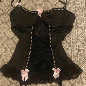Svart korsett med spets 🔥🔥🔥 - Snygg svart korsett med spetsdetaljer och söta rosa rosetter. Den har justerbara axelband.