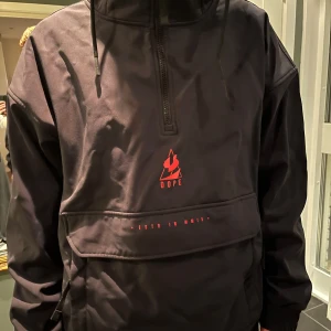 Svart skidjacka från Dope - Säljer en svart skidjacka från Dope i mycket bra skick. Den har en halv dragkedja och en stor ficka framtill men även fickor på sidorna.Perfekt för vintern och skidåkning med sin varma och skyddande design. Den har en stilren look med röd logga på bröstet.