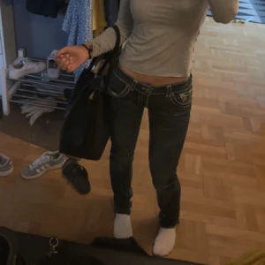 Mörkblå jeans från True Religion - Säljer ett par snygga mörkblå jeans från True Religion i storlek 29. De har en lågmidjad passform och är dekorerade med vita sömmar. Jeansen har en klassisk femficksdesign och knytdetalj i midjan. Perfekta för en casual look! Sömen har jag sprettat upp nere vid benen så dom ska bli längre. passar mig som är 1,66 ☺️