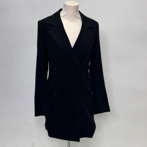 Svart kavaj klänning  - Snygg svart kavaj klänning i klassisk stil med dubbelknäppning. Perfekt för både formella och semi-formella tillfällen. Den har långa ärmar och en elegant passform som ger en stilren look.