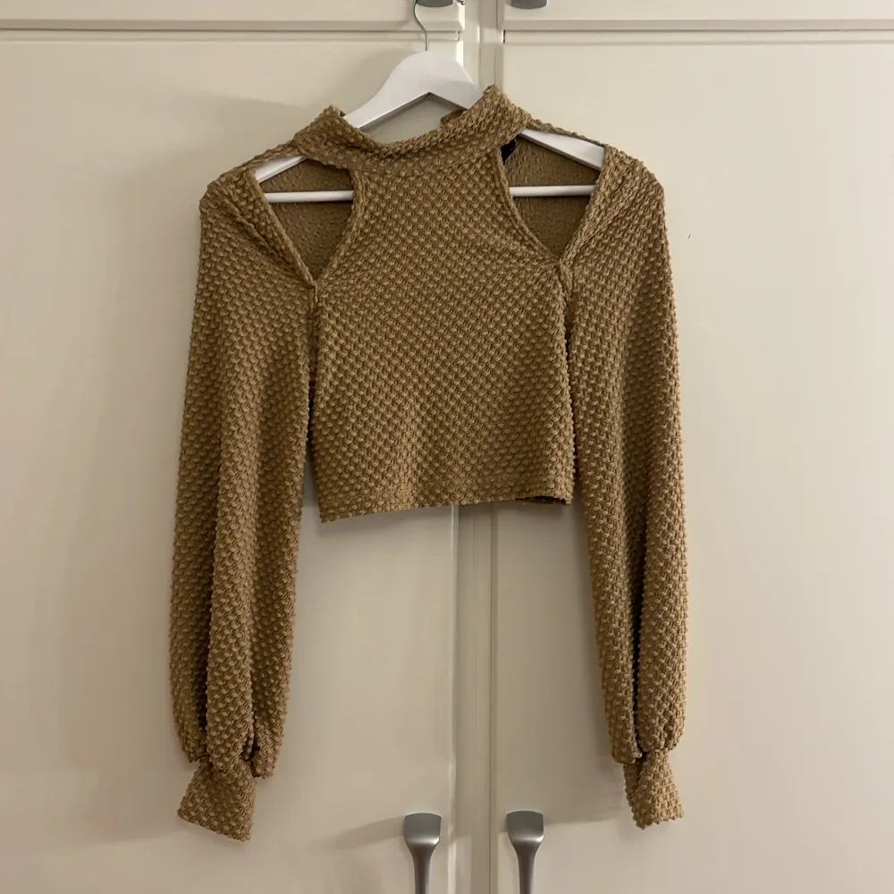 Säljer en superfin beige stickad tröja med coola cut-out detaljer vid axlarna. Den är croppad och har långa ärmar med ribbade muddar. Perfekt för höst och vår när du vill vara både varm och trendig. Passar perfekt till ett par höga jeans eller kjol!. Neuletakit & Villapaidat.