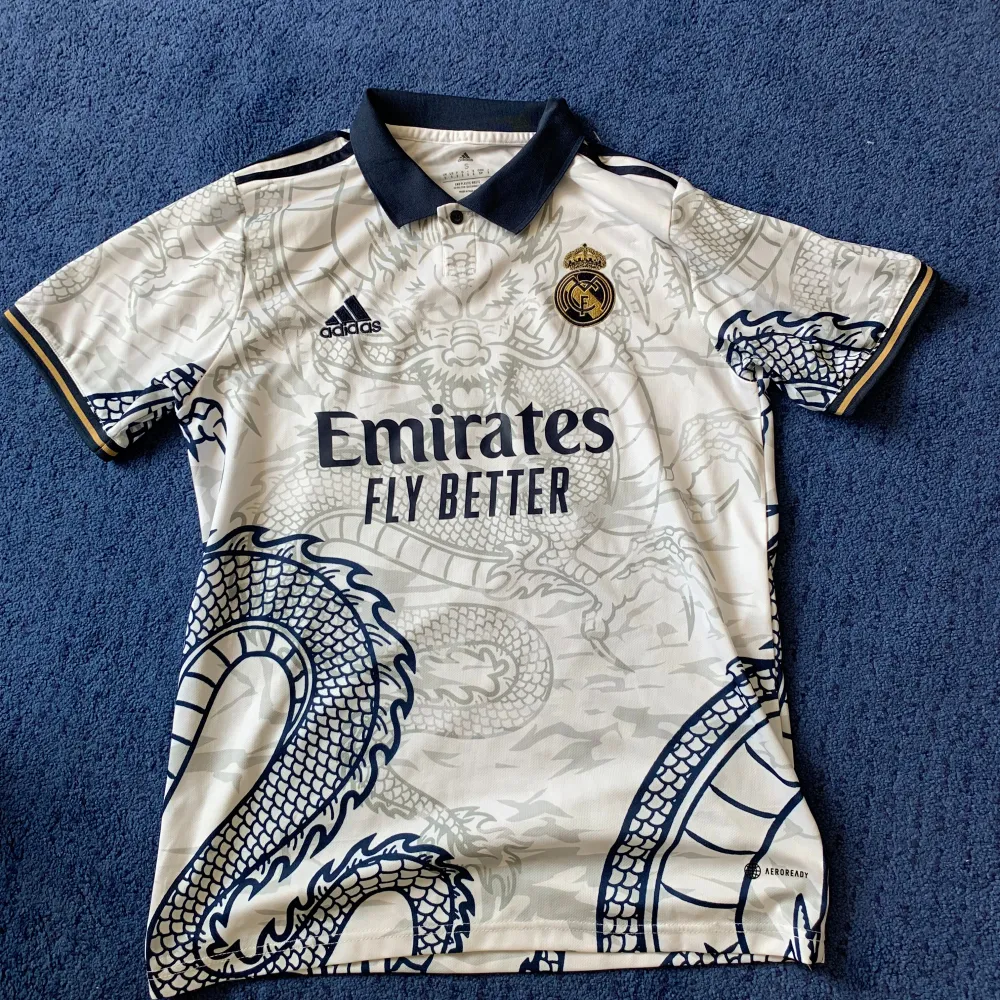 En överfet Real Madrid tröja i dragon special edition som är väldigt sällsynt att hitta. Tröjan är använd 1 gång så iprincip helt ny. Den har nummer 10 Modric på ryggen⭐️ Intresserad?. T-shirts.