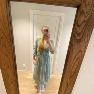 Grön blommig klänning från Shein - Säljer en superfin grön klänning från Shein med ett sött blommigt mönster. Klänningen har en v-ringad design och trekvartsärmar, perfekt för vår och sommar. Den är i storlek L och har en bekväm passform med volangdetaljer vid midjan. Perfekt för både vardag och fest!