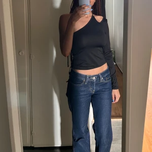 Svart one-shoulder - En svart one-shoulder crop top med en lång ärm. Denna topp är mångsidig och kan bäras både till casual tillfällen och festliga event.