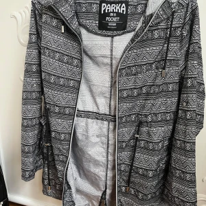 Svartvit mönstrad parka - Säljer en svartvit parka med ett unikt geometriskt mönster. Jackan har dragkedja och knappar framtill samt justerbar dragsko i midjan. Perfekt för att hålla stilen i alla väder! 🖤