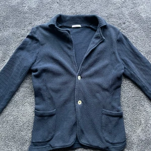 Mörkblå tröja från Knowledge Cotton Apparel - Snygg mörkblå kavaj/cardigan från Knowledge Cotton Apparel. Den har en stilren design och är perfekt för både en avslappnad och en uppklädd look. 