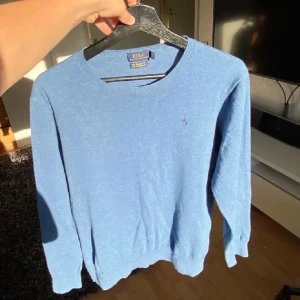 Ralph Lauren tröja - Säljer en stilren blå tröja från Polo Ralph Lauren. Tröjan har långa ärmar och en rund halsringning. Den är perfekt för en avslappnad och snygg look. Den ikoniska loggan är broderad på bröste.