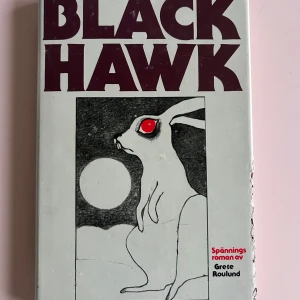 Black Hawk - Spännande roman av Grete Roulund med en mystisk och suggestiv omslagsbild av en hare med röda ögon framför en måne. Boken verkar handla om olycksbådande händelser och en grupp som inte kan undkomma sitt öde. Perfekt för dig som gillar spänning och mystik. Men kanin har tuggat på ena omslagets sida men boksidorna är i toppskick.