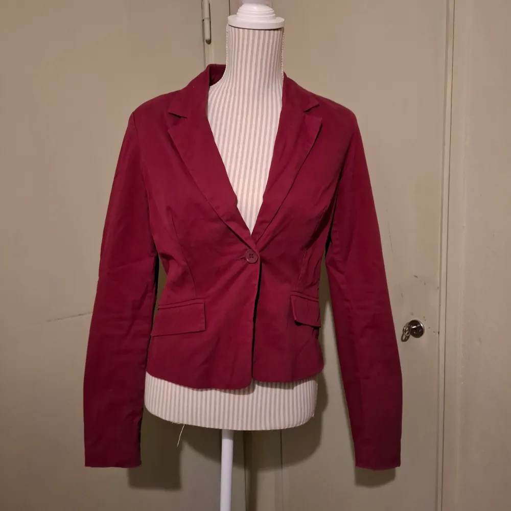 Snygg vinröd kavaj från Top Secret i storlek 38. Kavajen har en klassisk design med en knapp framtill och långa ärmar med tre knappar vid ärmsluten. Perfekt för en stilren look.. Takit.