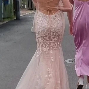 Rosa långklänning med spetsdetaljer - Elegant rosa långklänning med vackra spetsdetaljer och snörning i ryggen. Klänningen har en figurnära passform och är perfekt för speciella tillfällen. Den har en romantisk känsla med sina blommiga mönster. Med snörningen passar den även 34 vilket jag är på bilderna. Passar även vilken kupa som helst 