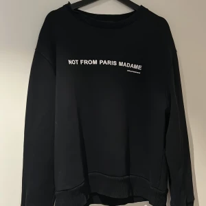 Svart sweatshirt från Drôle de Monsieur - Använd men helt ok skick. Svart sweatshirt från Drôle de Monsieur med texten 'Not From Paris Madame' på bröstet. Tröjan har långa ärmar och ribbade muddar vid ärmslut och nederkant. Perfekt för en stilren och avslappnad look. Passar M/L