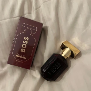 OÖPPNAD Boss The Scent Elixir Parfym - OÖPPNAD Elegant parfym från Hugo Boss, The Scent Elixir. Flaskan är mörk med en lyxig guldlock, vilket ger en exklusiv känsla. Förpackningen är vinröd med guldtext, vilket förstärker den sofistikerade stilen. Perfekt för den som vill ha en doft med karaktär.