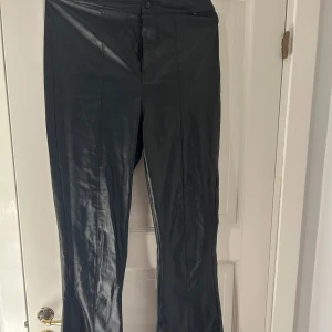 Svarta byxor från Boohoo - Snygga svarta byxor från Boohoo i ett glansigt material. De har en hög midja och utsvängda ben. Dem är knappt andvända men tyvärr har knappen blivit lite lös. 