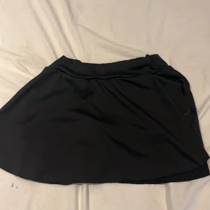 Svart kjol med shorts - Snygg svart kjol med inbyggda shorts, perfekt för en aktiv dag. Kjolen har en enkel design med en bekväm passform och praktiska fickor. Materialet är mjukt och stretchigt för extra komfort.