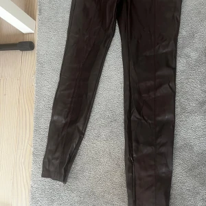 Bruna skinnbyxor från Zara - Snygga bruna skinnbyxor från Zara i storlek M. Byxorna har en tight passform och är utrustade med dragkedja vid bensluten för extra stil. Perfekta för en trendig look.