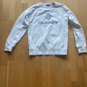 Vit sweatshirt från GANT - Säljer en stilren vit sweatshirt från GANT med deras ikoniska logotyp broderad i blått på framsidan. Storlek: 146/152